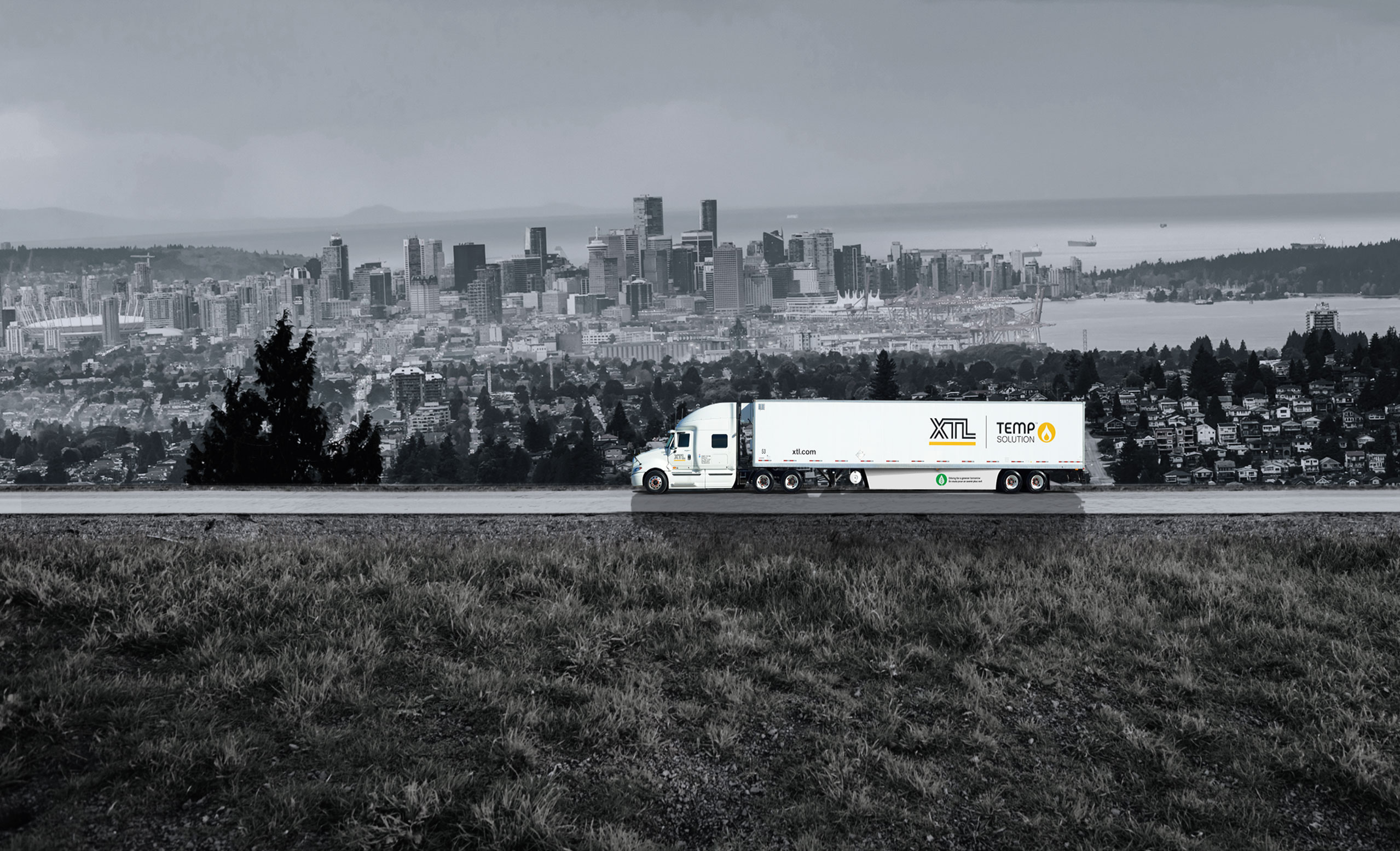 XTL transport truck and trailer driving on road, with city of Vancouver in the background